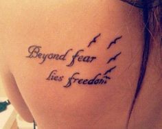 the back of a woman's shoulder with a tattoo saying, beyond fear lies freedom