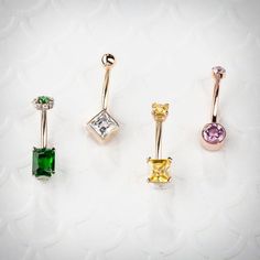 four different colored jeweled piercings on a white surface, one is yellow and the other is green