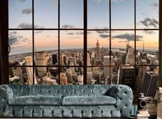 a blue couch sitting in front of a window with the view of a large city