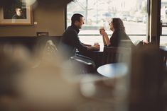 two people sitting at a table in a restaurant drinking coffee and talking to each other