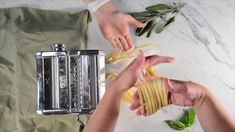 two hands are peeling pasta on a marble counter top, while another person is holding a silver toaster