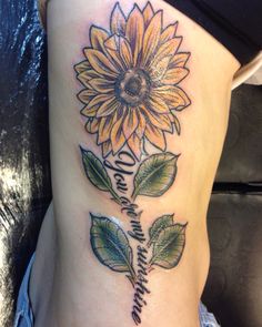 a sunflower tattoo on the side of a woman's stomach with words written in cursive writing