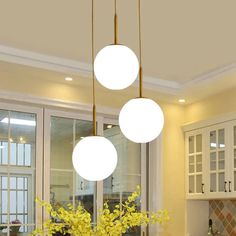 three lights hanging from the ceiling above a kitchen island with yellow flowers in vases