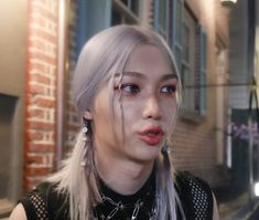 a woman with white hair and piercings standing in front of a brick building