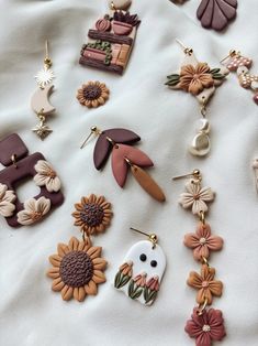 many different earrings are laying on a white sheet with flowers and other items in the background