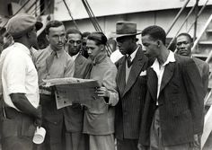 a group of men standing around each other in front of a boat on the water