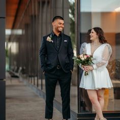 a man and woman standing next to each other in front of a building with glass doors