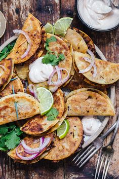 some tacos are on a plate with sour cream and cilantro wedges