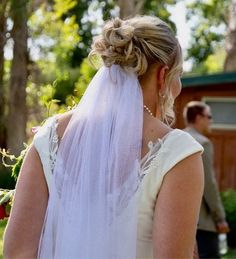 the back of a bride's dress with a veil on her head and flowers in her hair