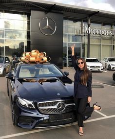 a woman standing next to a black car with a bow on it's roof