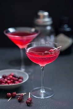 two wine glasses filled with cranberry martinis and cherries on the table