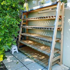 a wooden shelf sitting on top of a patio next to a bush and tree with lots of green leaves