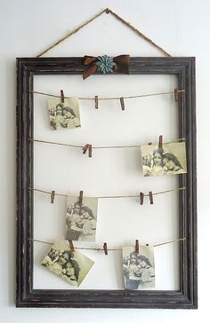 an old photo frame hanging on a wall with clothes pins attached to it and pictures pinned to the rope