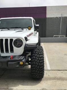 a white jeep parked in a parking lot next to a purple and black building with a sign on it