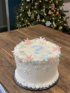 a frosted cake sitting on top of a wooden table next to a christmas tree