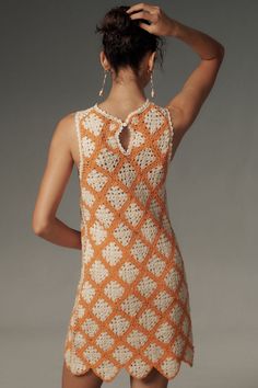 a woman in an orange and white crochet dress with her back turned to the camera