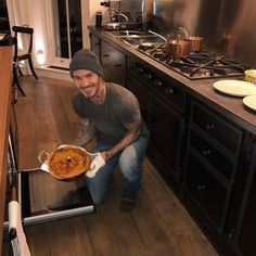 a man holding a pan filled with food on top of a wooden floor in a kitchen