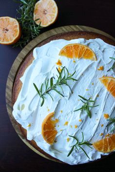 a cake with oranges and rosemary on top sitting on a wooden plate next to an orange slice