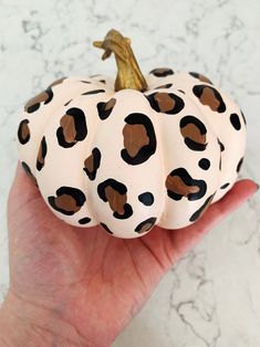 a hand holding a white and black painted pumpkin with leopard print on it's skin