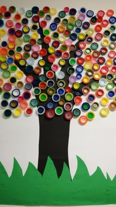 a tree made out of bottle caps on a bulletin board with grass and trees in the background