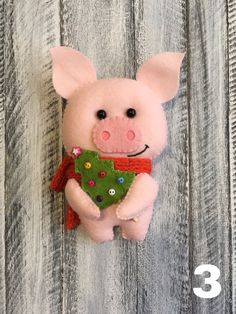 a stuffed pig holding a green christmas tree ornament on a wooden background with text overlay