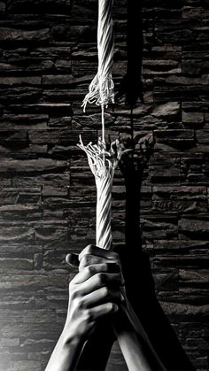 two hands holding up a rope with one hand and the other in the air, against a stone wall