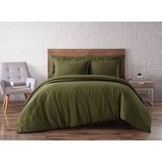 a bed with green sheets and pillows in a room next to a white brick wall