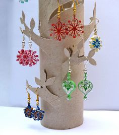 several colorful earrings are hanging from a paper tube in the shape of a tree with leaves and flowers on it