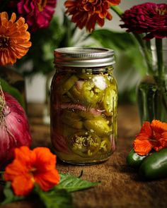 pickles and flowers sit on a table next to a jar of pickled peppers