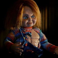 a creepy doll with red hair and blue eyes is posed in the dark, looking at the camera