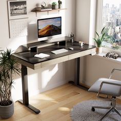 a desk with a computer on it in front of a window and a potted plant