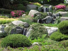 a garden with large rocks and water fall in the center, surrounded by plants and flowers