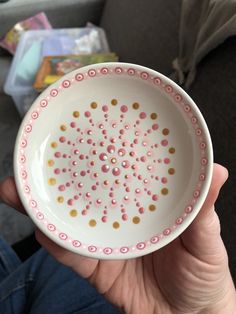 a person holding a white bowl with pink and gold dots on it in their hand