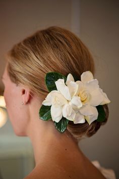 a woman with blonde hair wearing a white flower and green leaves in her hair is looking into the mirror