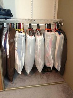 there are many bags hanging on the rack in this closet, and one bag is filled with clothes