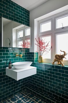 a bathroom with green tiles and a white sink in front of a window that has an elephant figurine on the ledge