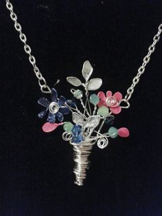 a silver necklace with flowers and leaves on the front is hanging from a black background