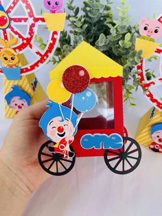 a hand holding up a small toy house with balloons on it's wheels and other decorations