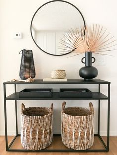 two wicker baskets under a table with a mirror and vases on the side