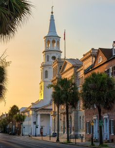 an old building with a steeple and palm trees on the street in front of it