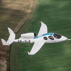 a small white airplane flying over a lush green field