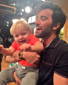 a man holding a little boy in his arms while he smiles at something on the floor