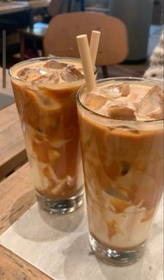 two glasses filled with iced coffee sitting on top of a wooden table next to each other