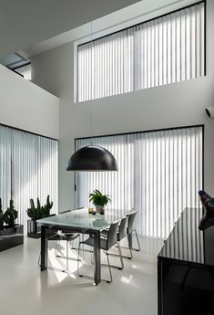 a modern dining room with white walls and flooring, along with large windows that have vertical blinds on them