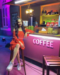 a woman sitting on a stool in front of a coffee shop with neon lights behind her