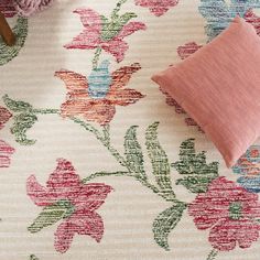 a pink pillow sitting on top of a white rug next to a vase with flowers