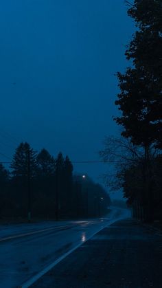 an empty street at night with no cars on the road and trees in the background