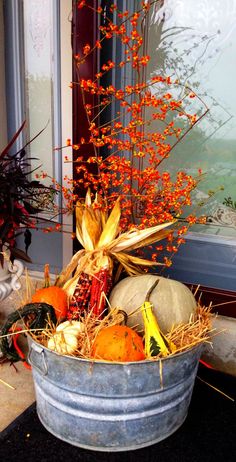 a bucket filled with pumpkins and gourds next to a window