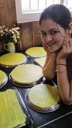 a woman sitting in front of some pies on a table with yellow frosting