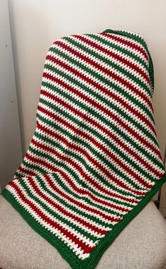 a green and red striped blanket sitting on top of a chair next to a white wall